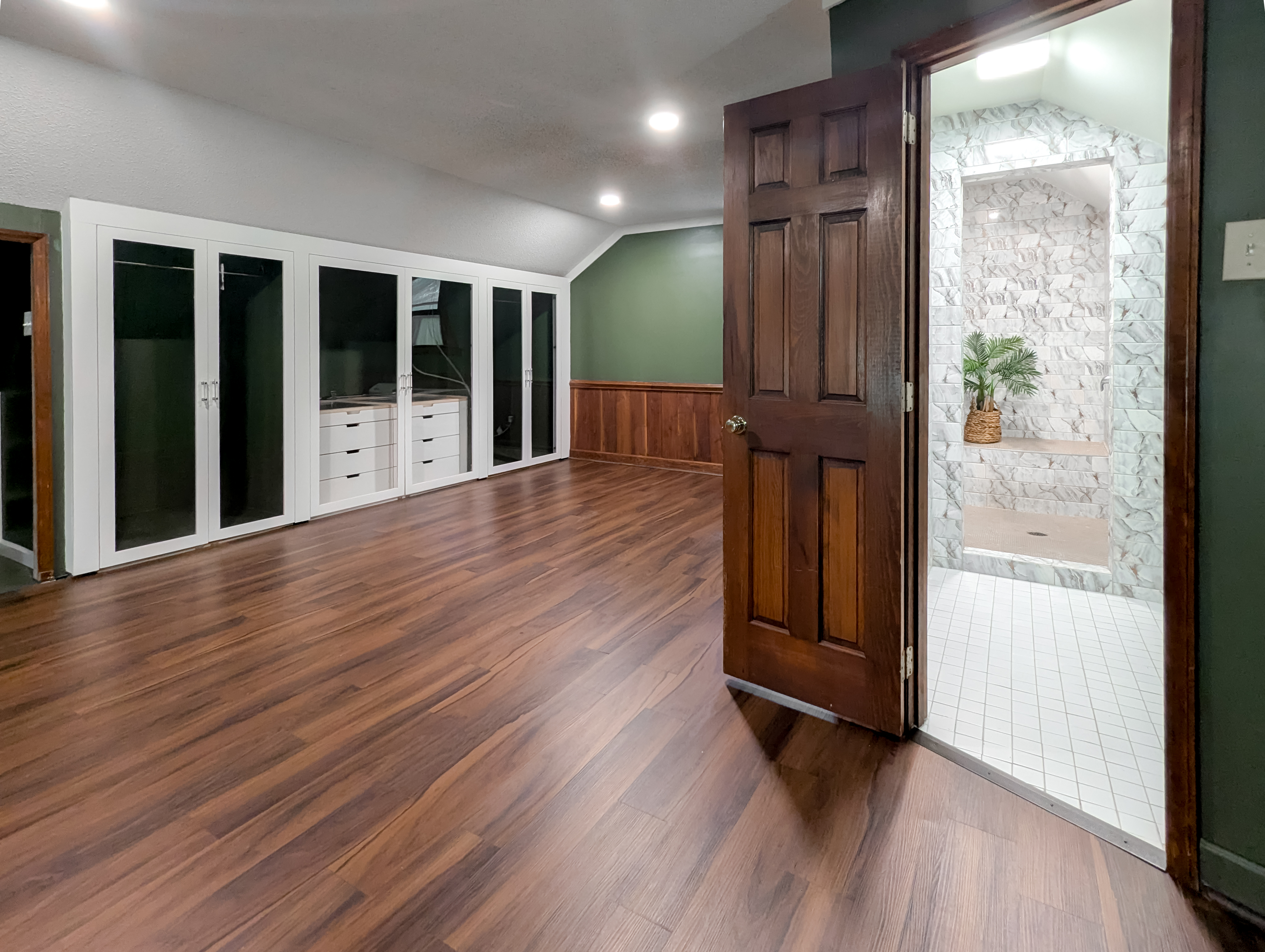 Upper-level suite with wood-look floors, built-in glass-front closet and an open full bath beyond
