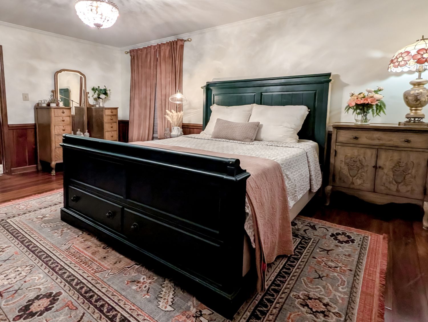 Primary bedroom with a dark sleigh bed, antique dressers, layered rugs and an ensuite bathroom visible through the doorway